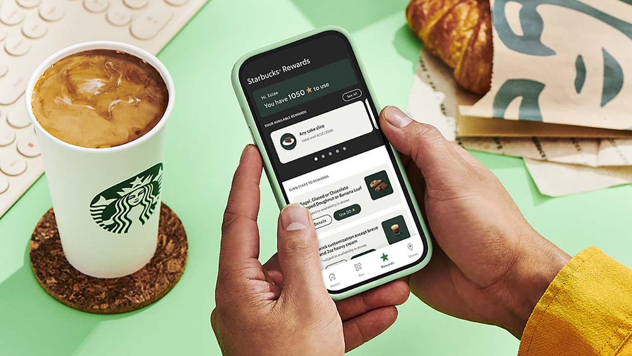 A hand holding a phone showing the Starbucks Rewards screen with a Star balance