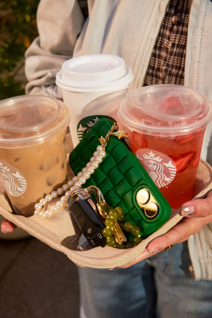 A tray of Starbucks drinks held in one hand alongside car keys and a green phone case